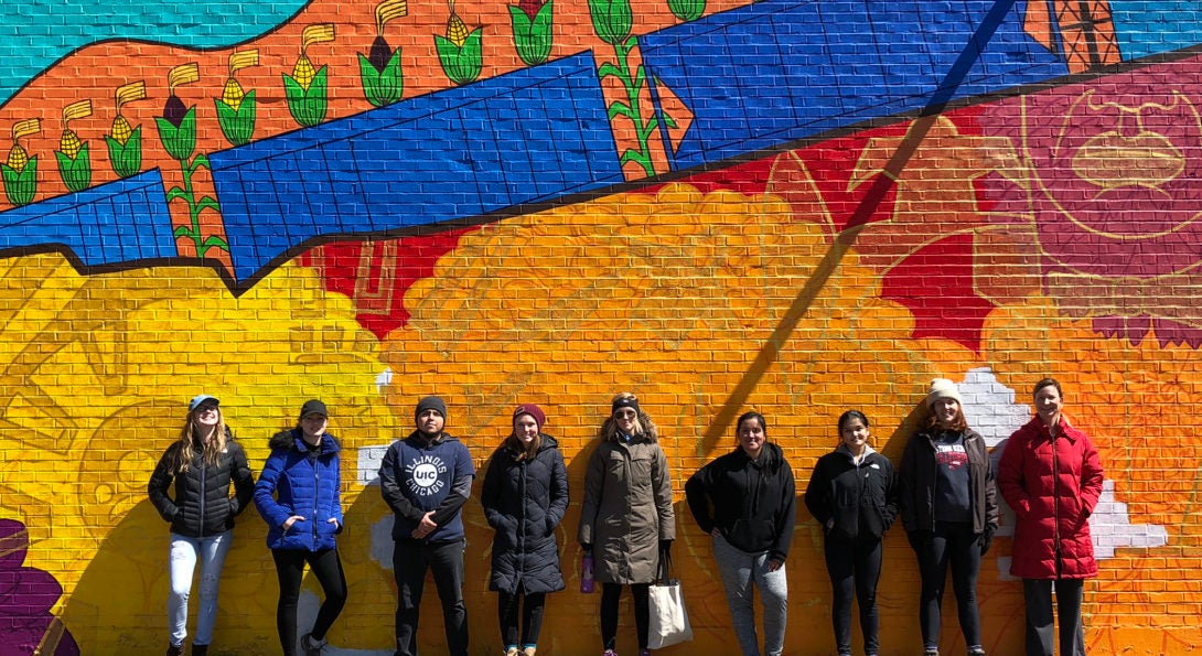 UIC volunteers at El Paseo Community Garden stand in front of a mural