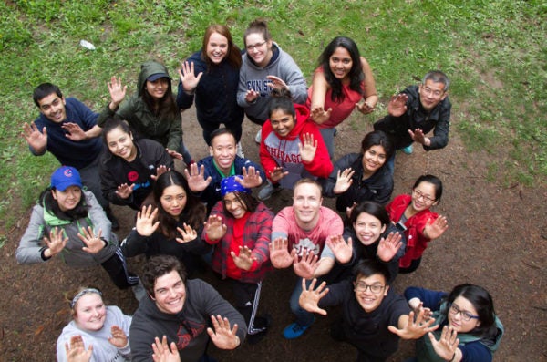 Group of people looking up at camera from below, with arms raised and palms open, smiling