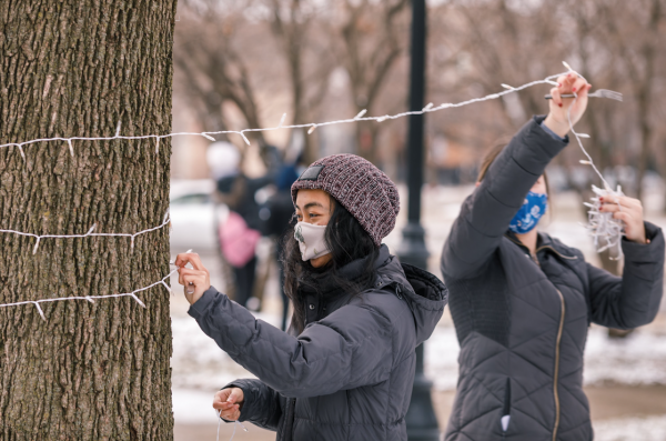 Volunteer in mask removing string of lights from tree in winter