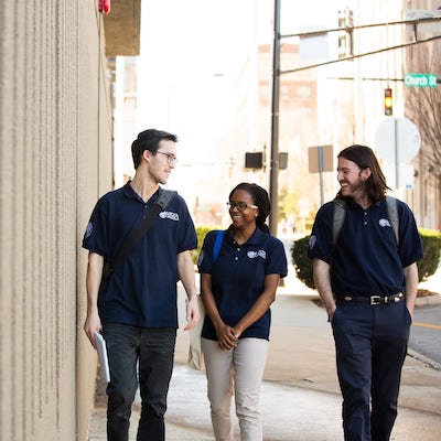 Three people in AmeriCorps VISTA Volunteer navy blue polos walking and smiling at each other